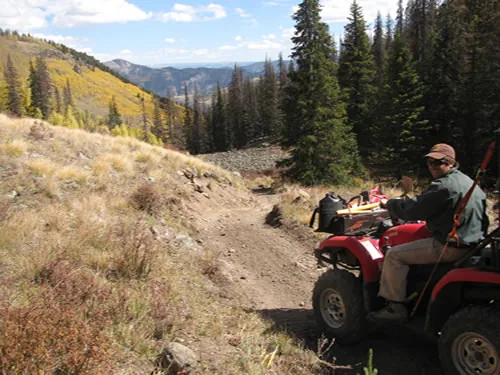 Person on a four-wheeler pausing on a mountain trail above a valley of golden autumn aspens and distant ridges
