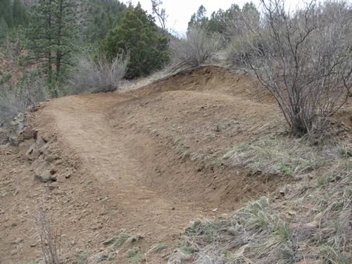 Wide bermed switchback turn shaped in fresh dirt on a hillside, with a forested slope behind