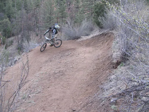 Mountain biker riding through a wide bermed turn on a hillside trail above a wooded drainage