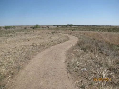 Crusher fine path curving through open prairie grassland toward a distant line of trees